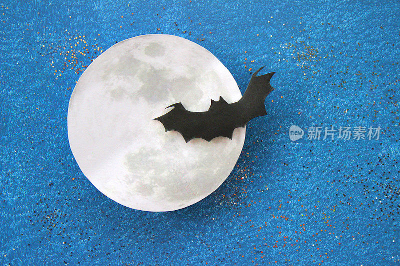 黑色蝙蝠的剪影在纸月亮前飞行，万圣节村庄/万圣节的背景